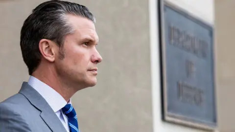 EPA-EFE/REX/Shutterstock Side shot of Pete Hegseth's head next to to a sign that says Department of Defense. He is wearing a light grey suit, light shirt and a dark blue tie with light blue stripes.